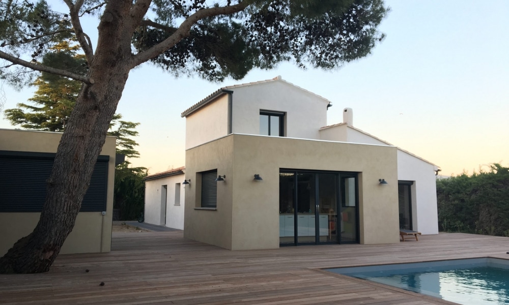 Maison moderne bicolore avec piscine, grande terrasse en bois et pin parasol au crépuscule.