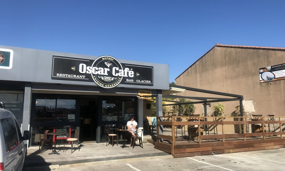 Devanture du restaurant Oscar Café avec sa terrasse en bois et mobilier extérieur par temps clair.