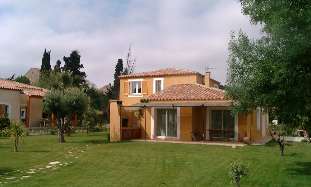 Villa provençale ocre avec toit de tuiles, pelouse verte et oliviers sous un ciel clair.