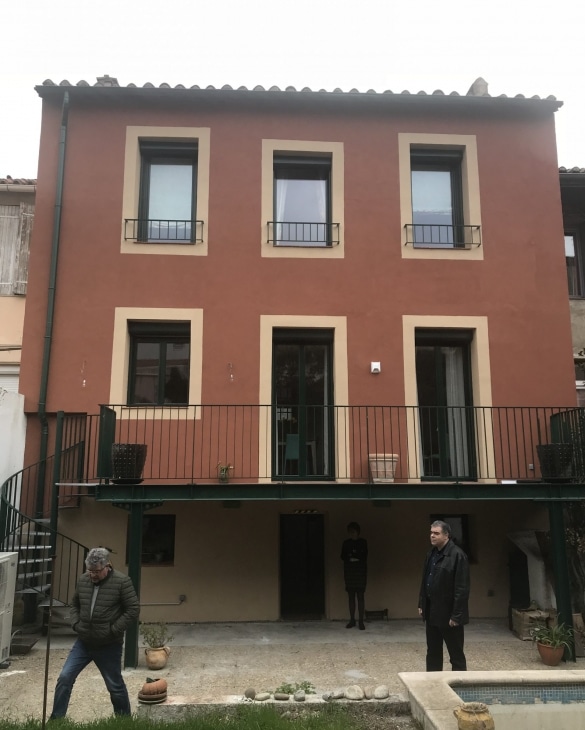 Maison terre cuite, balcon métallique, escalier colimaçon et personnes dans la cour.