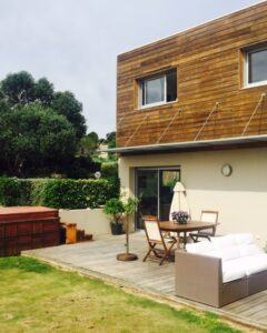 Terrasse en bois avec spa, mobilier de jardin et canapé blanc devant une maison moderne.