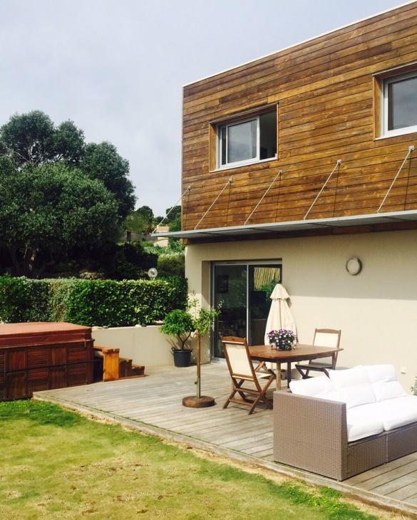 Terrasse en bois avec spa, mobilier de jardin et canapé blanc devant une maison moderne.